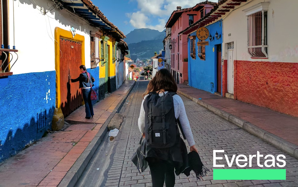 Devcon VI in Bogotá: CSO Ryan Lackey Examines the Past Three Years in Web3 Security Image of a small road with colorful buildings on each side. There are two women in the photo, one is opening a door and the other is walking down the small road with a large backpack. The city overlooks mountains meeting clouds in the blue sky.