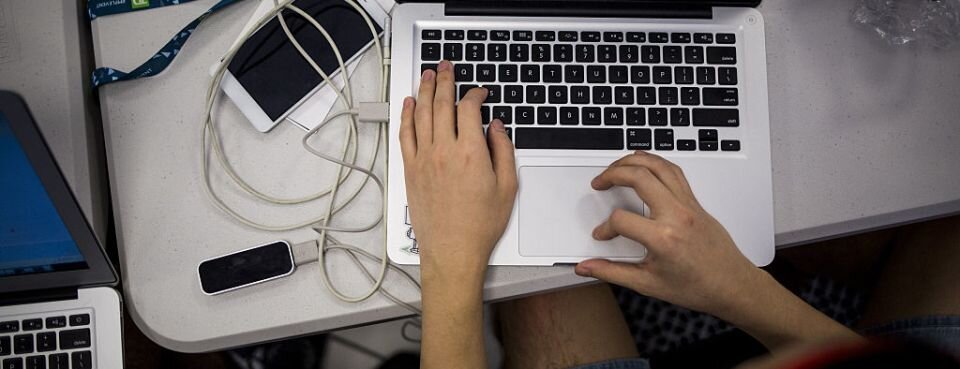 Wake Up Call: David Lat, Founder of Above the Law, Says He Has Covid-19 Persons hands typing on a laptop keyboard with USB cord running to what looks like an external hard drive. There is also a cellphone sitting next to the computer on the desk its sitting on.